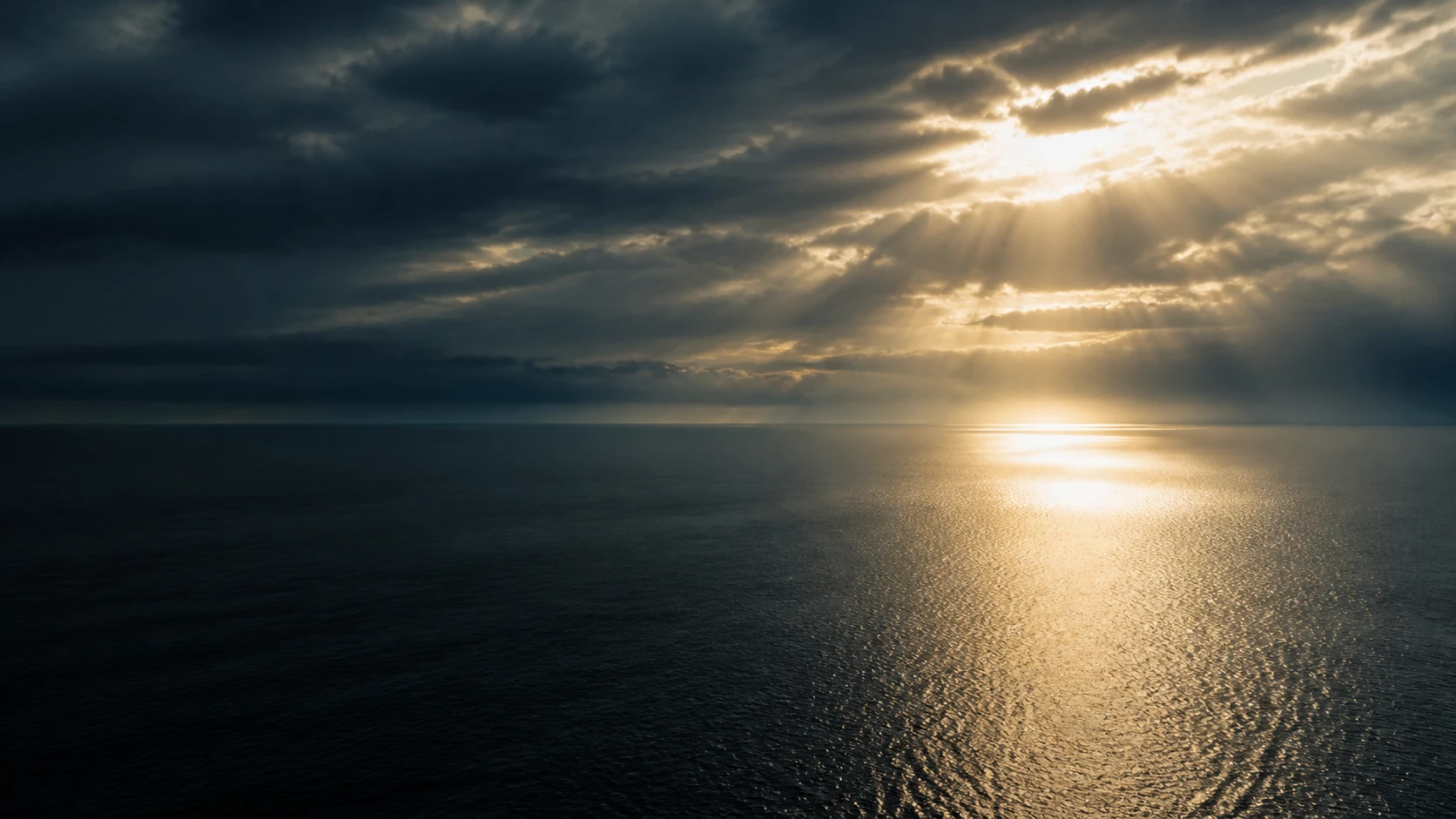 Sunlight breaks through clouds over a still lake at first light.